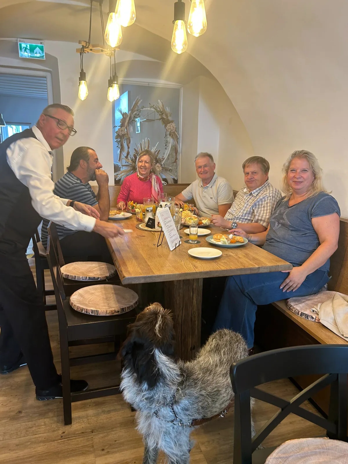 G&auml;ste mit Hund an einer gedeckten Tafel im Gastraum